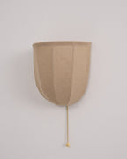 Front view of an unlit Clérachic linen wall sconce with a smooth beige shade and a beaded chain on a pale wall.