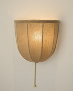 Large close view of a lit Clérachic linen wall sconce, with the glowing shade and a brass pull chain on a cream wall.