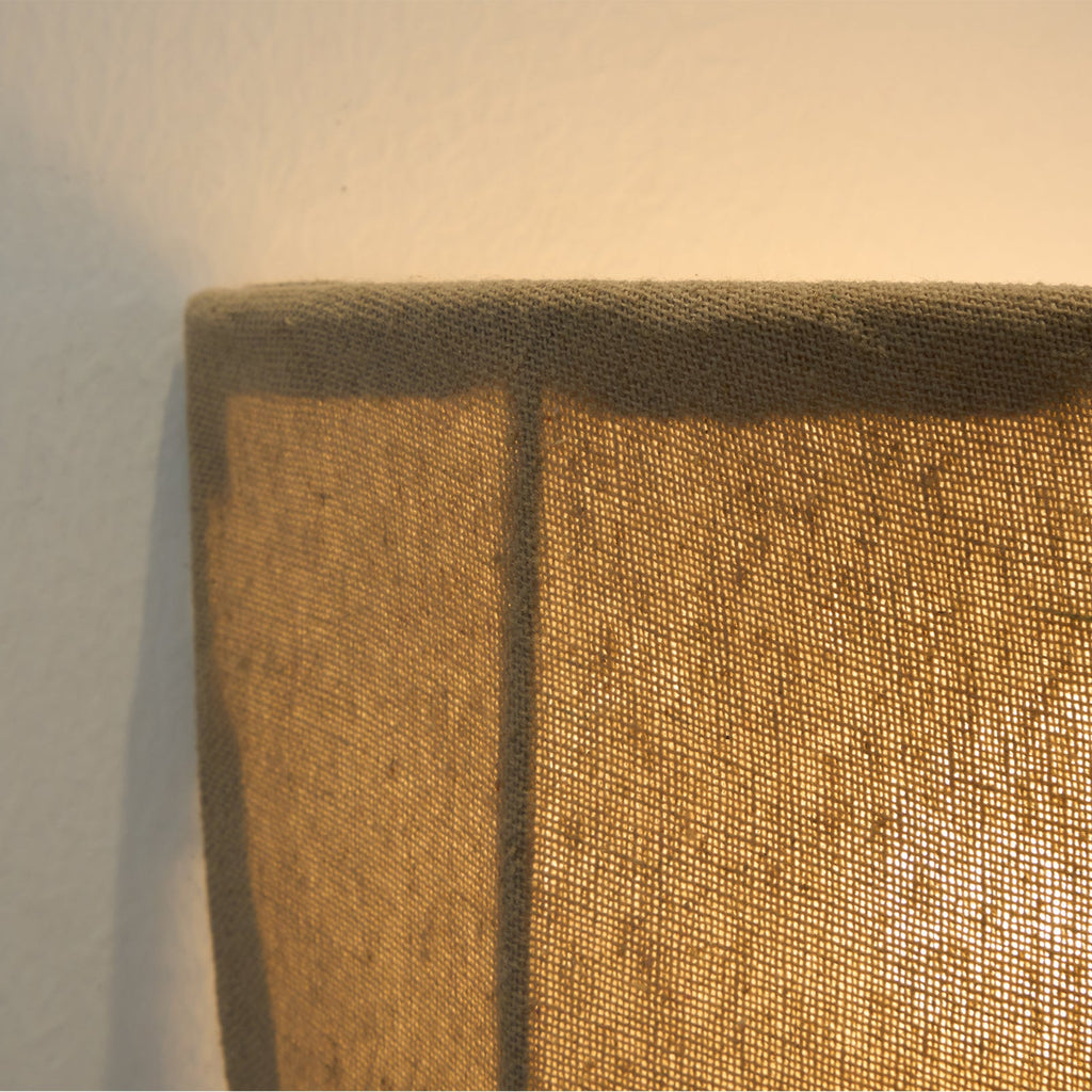 Close view of the stitched linen rim and a dark seam on a lit Clérachic wall sconce.