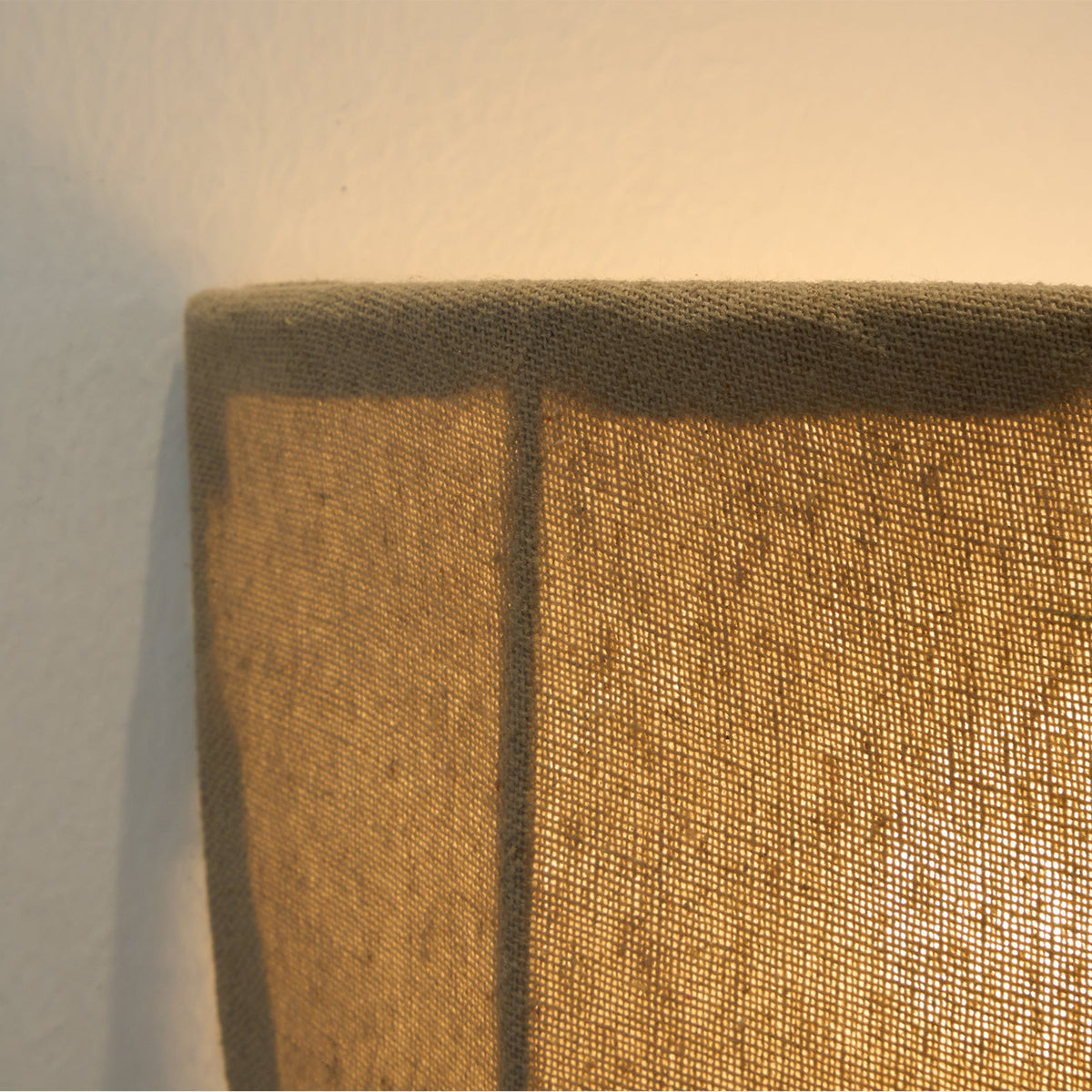 Close view of the stitched linen rim and a dark seam on a lit Clérachic wall sconce.