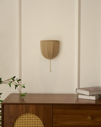 Small Clérachic linen wall sconce on a panelled cream wall above a walnut cabinet with a cane door and stacked books.
