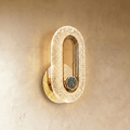 Clérachic gold oval wall lamp with a patterned acrylic band and a round blue-green stone inlay, glowing on limewash.