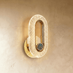 Clérachic gold oval wall lamp with a patterned acrylic band and a round blue-green stone inlay, glowing on limewash.