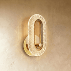 Clérachic gold oval wall lamp with a lit faceted acrylic band and a plain brass knob in the opening, on limewash.