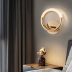 Clérachic gold ring wall lamp glowing above a bedside table with a figurine, beside grey curtains and a bed.