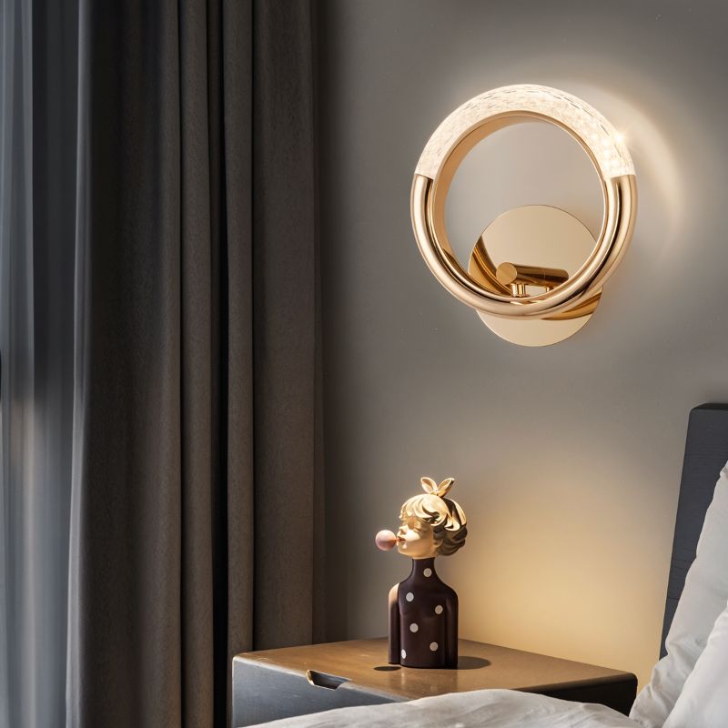 Clérachic gold ring wall lamp glowing above a bedside table with a figurine, beside grey curtains and a bed.