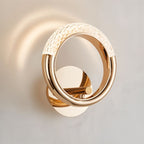 Close view of the Clérachic polished gold ring wall lamp, its pebbled acrylic arc glowing on a pale wall.