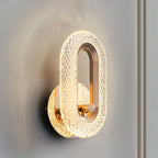 Close view of the Clérachic gold oval wall lamp, its faceted crystal-effect acrylic band lit against a grey wall.