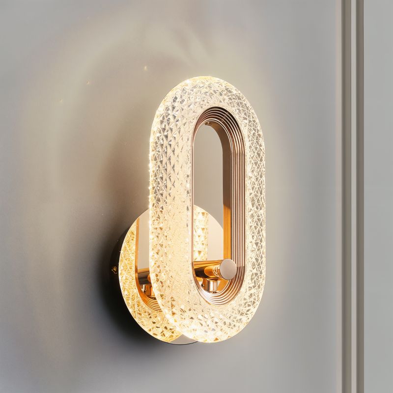 Close view of the Clérachic gold oval wall lamp, its faceted crystal-effect acrylic band lit against a grey wall.
