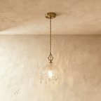 Clérachic pendant lamp with a cut-glass dome, crystal drops and a gold canopy on a twisted cord, lit warm.