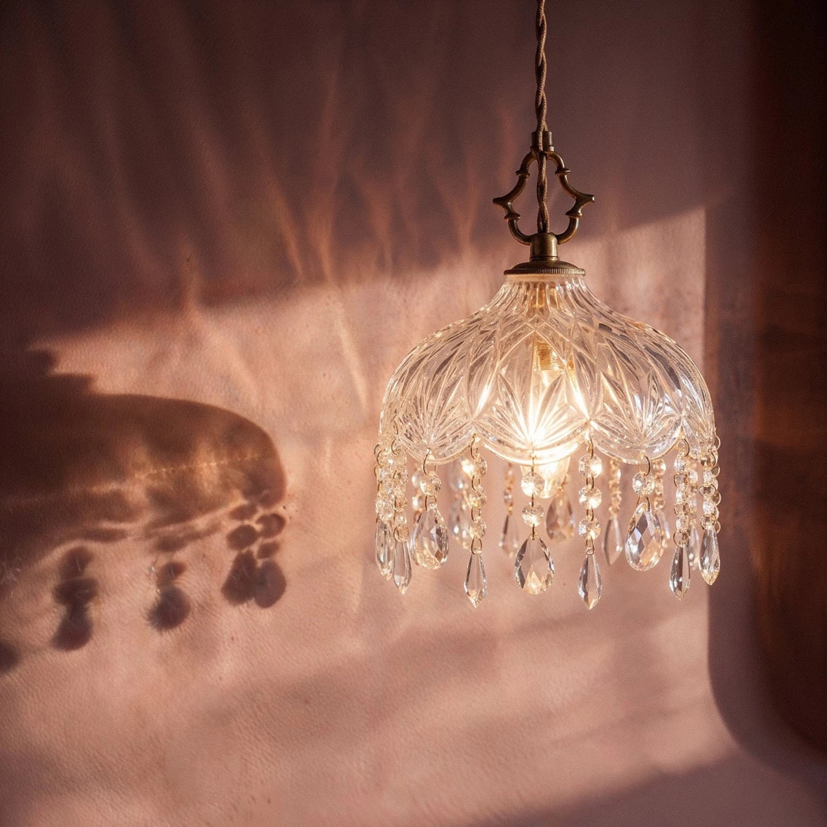 Close view of a Clérachic pendant lamp: faceted glass dome, gold fittings and crystal drops casting soft shadows.