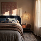 Clérachic gold wall lamp with a crystal-fringed glass shade lit beside a bed and a walnut bedside table.