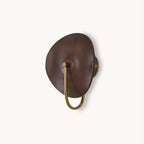 A Clérachic wall light with a walnut-colour wood disc and a gold U-shaped arm, on a plain off-white backdrop.