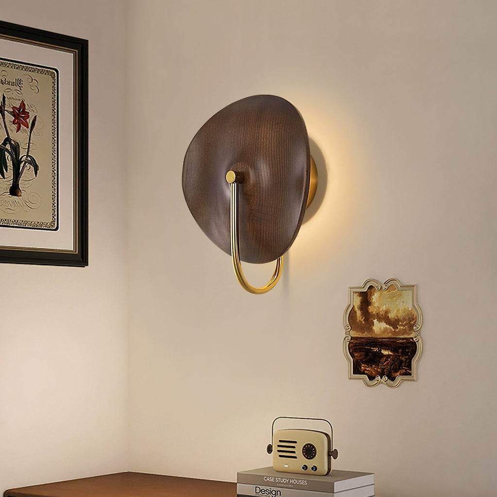 Warm light glows around the walnut-colour disc of this Clérachic wall light, mounted in a corner above a wooden sideboard and a small radio.