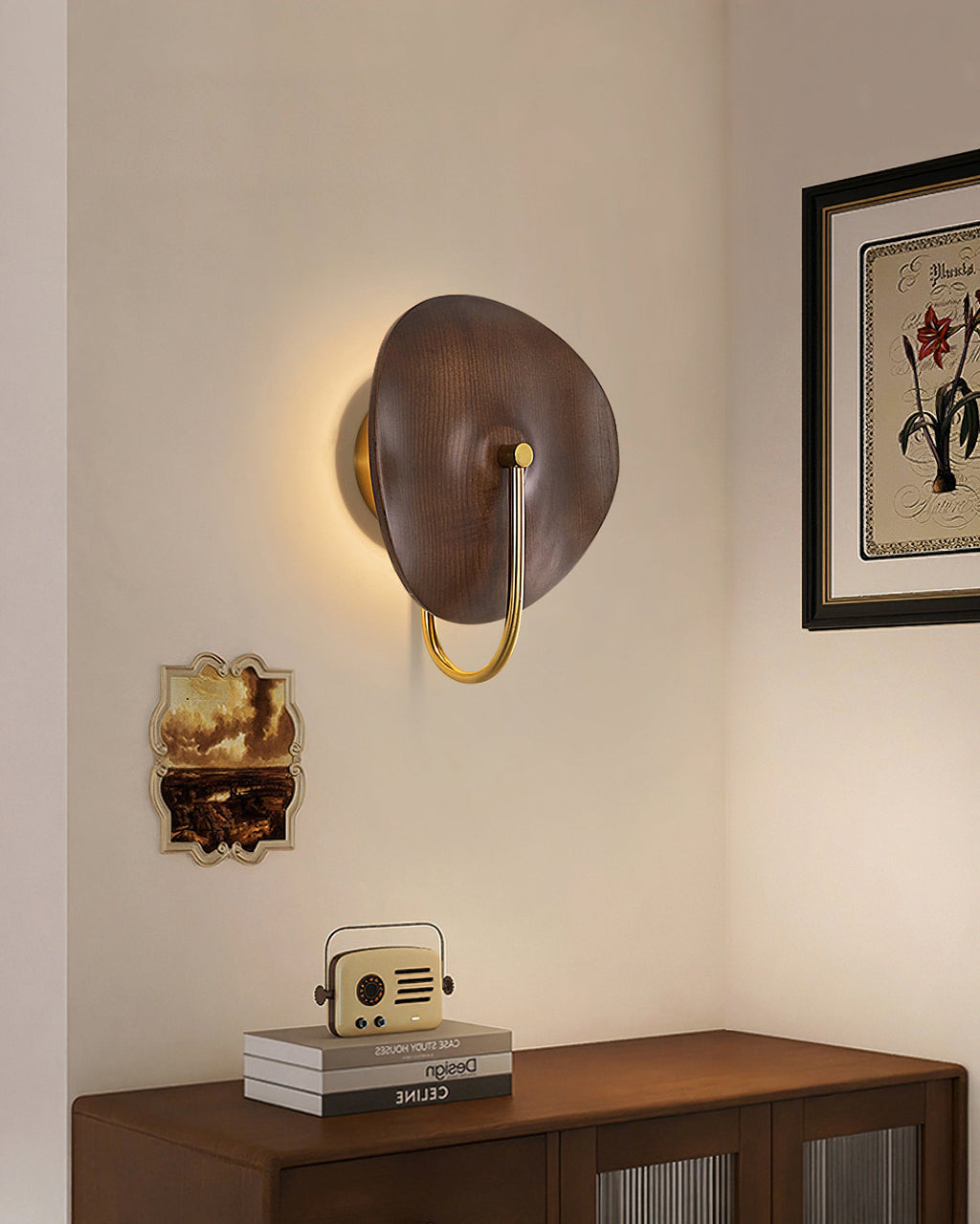 From a wider angle, a Clérachic walnut-colour wall light glows on a beige wall above a wooden cabinet, next to a framed botanical print.