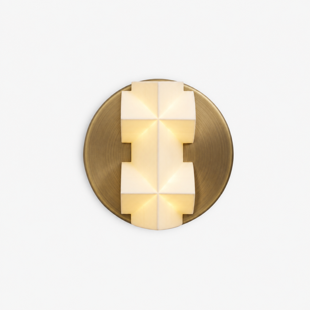 Front view of a lit Clérachic wall sconce, a white faceted shade with spear-like points on a round gold backplate, on a white backdrop.