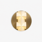 Front view of a lit Clérachic wall sconce, a white faceted shade with spear-like points on a round gold backplate, on a white backdrop.