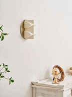 Side view of an unlit cream Clérachic wall sconce, its two curved points projecting from a gold disc, with a leafy branch at the left.