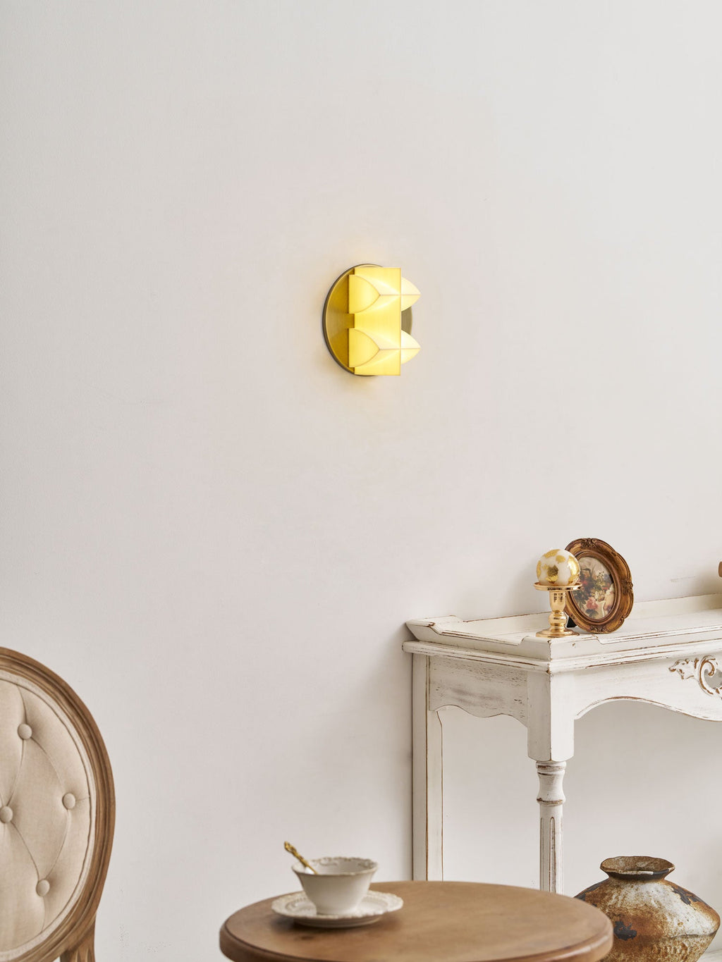 A small yellow glow from this Clérachic sconce, seen side-on above a white console with a gilt ornament and a teacup.