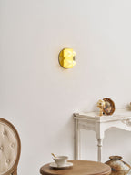 A small yellow glow from this Clérachic sconce, seen side-on above a white console with a gilt ornament and a teacup.