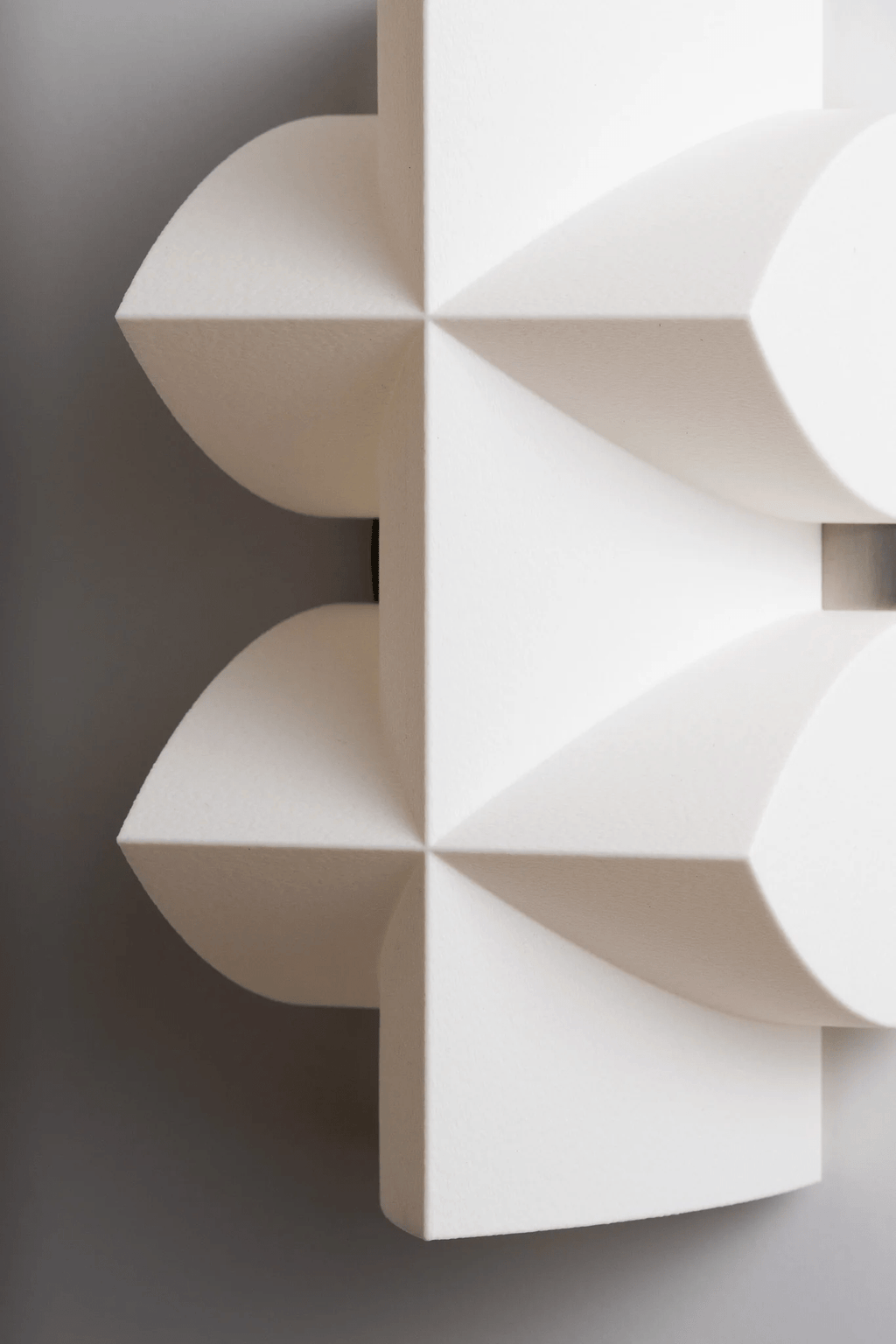 Close view of the white faceted shade, with its curved points and crossed ridges, on this Clérachic wall sconce.