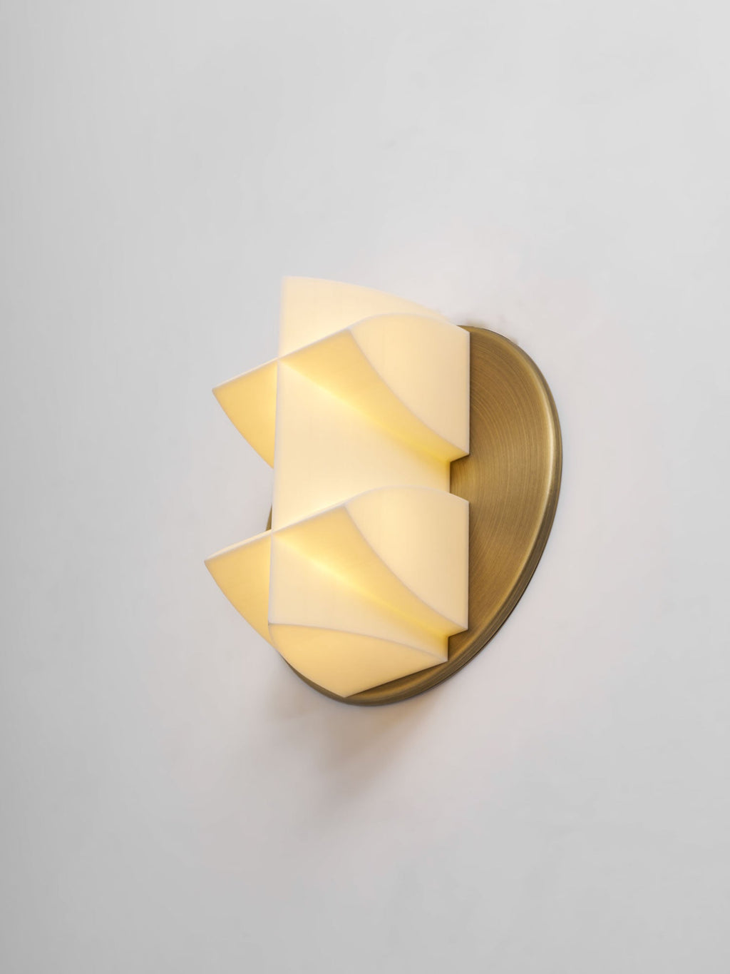Three-quarter view of a Clérachic wall sconce, its white faceted shade lit from inside and its points reaching out from a gold disc.