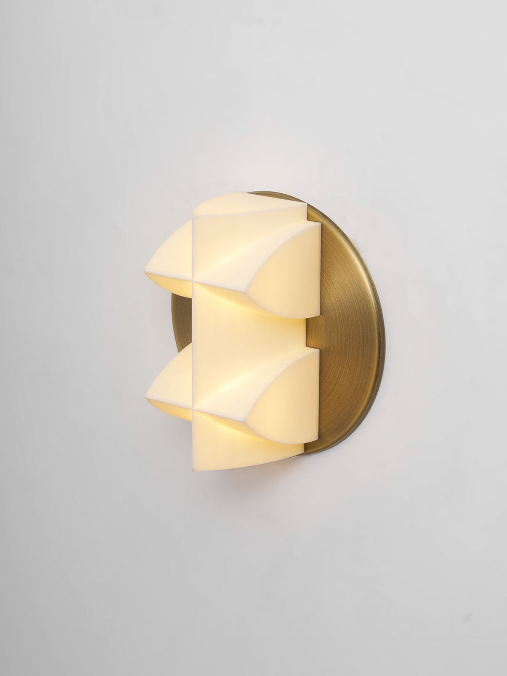 Lit Clérachic sconce seen at an angle, warm light spilling through the white facets beside a gold backplate.