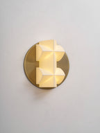 A Clérachic wall sconce glowing from within, its white facets set slightly off-centre on a brushed gold disc.