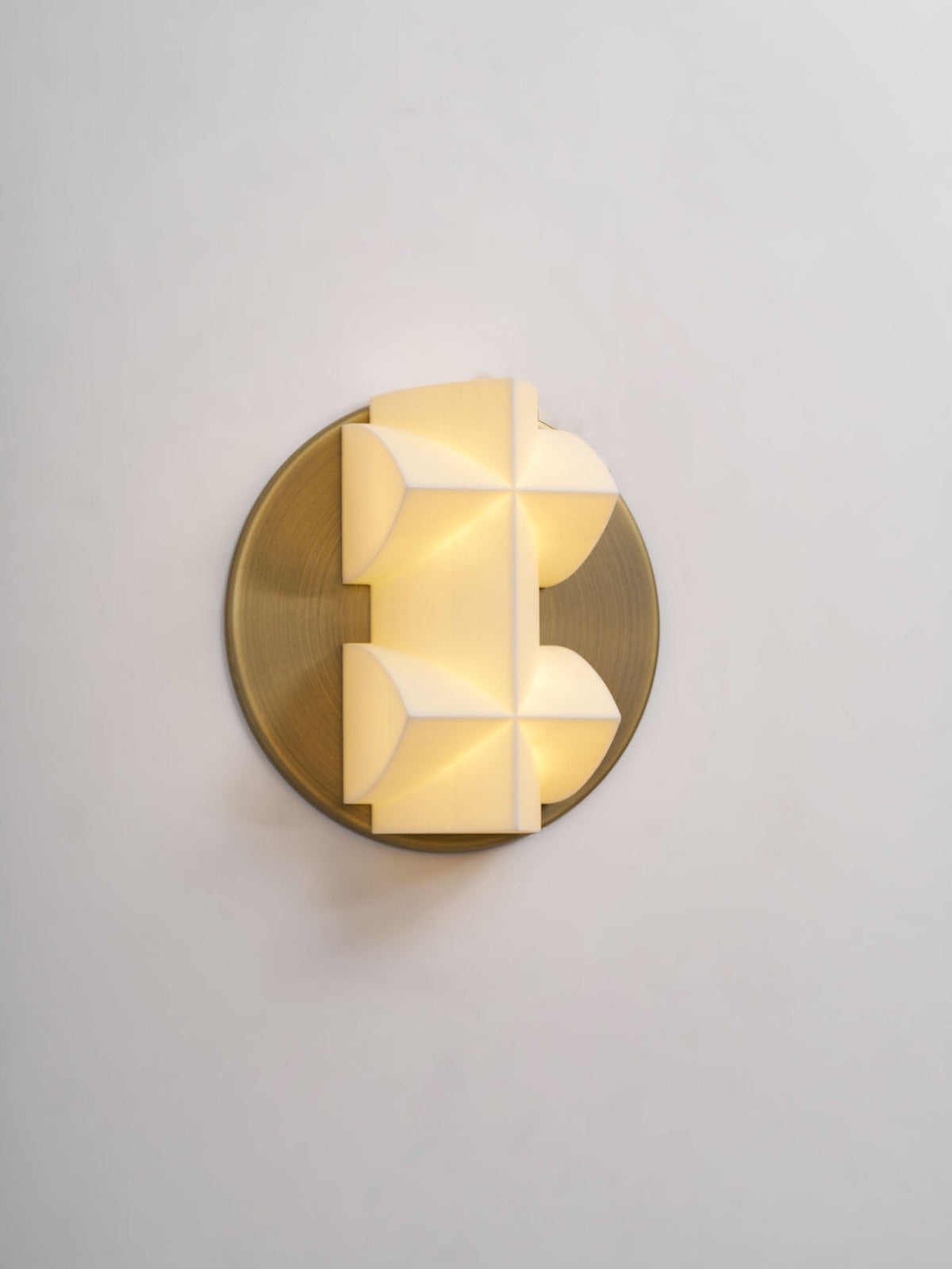 A Clérachic wall sconce glowing from within, its white facets set slightly off-centre on a brushed gold disc.