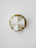 A single white crossed-facet shade, unlit, on a round gold backplate of this Clérachic sconce, on a textured white wall.