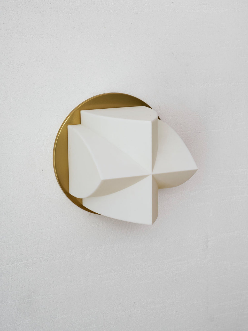 Angled close view of an unlit white Clérachic sconce with a single curved point turned to the right, on a gold disc.