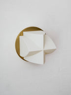 Angled close view of an unlit white Clérachic sconce with a single curved point turned to the right, on a gold disc.