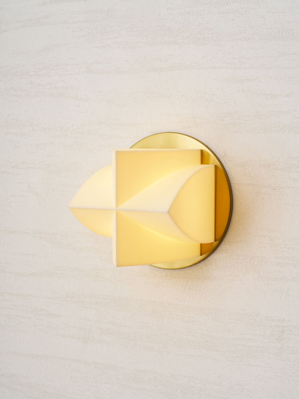 A Clérachic wall sconce lit warm, seen from the left, with a soft yellow glow through its white facets.