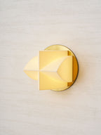A Clérachic wall sconce lit warm, seen from the left, with a soft yellow glow through its white facets.
