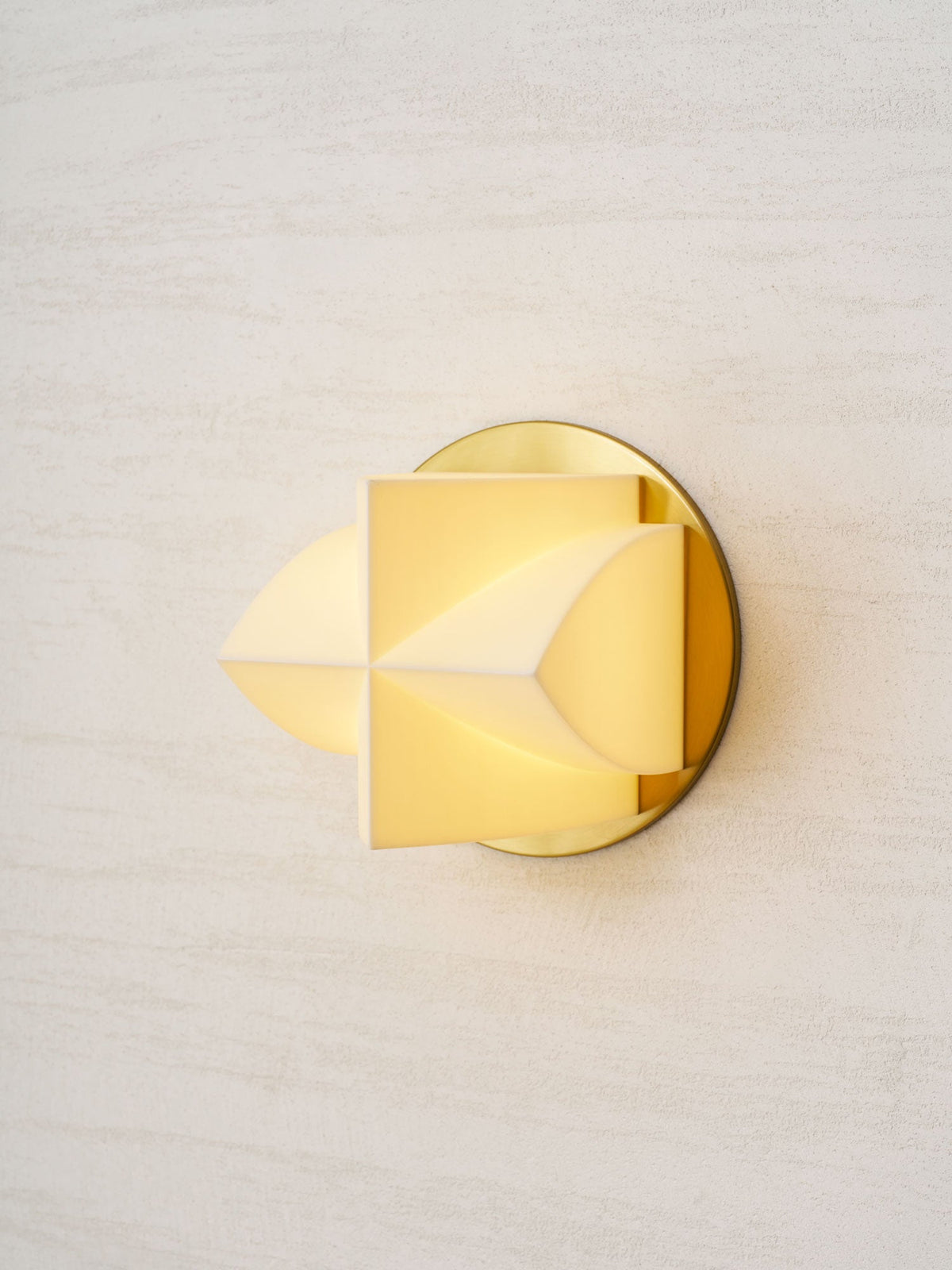 A Clérachic wall sconce lit warm, seen from the left, with a soft yellow glow through its white facets.