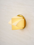 Close angled view of a lit Clérachic wall sconce, its white facets glowing yellow in front of a gold backplate.