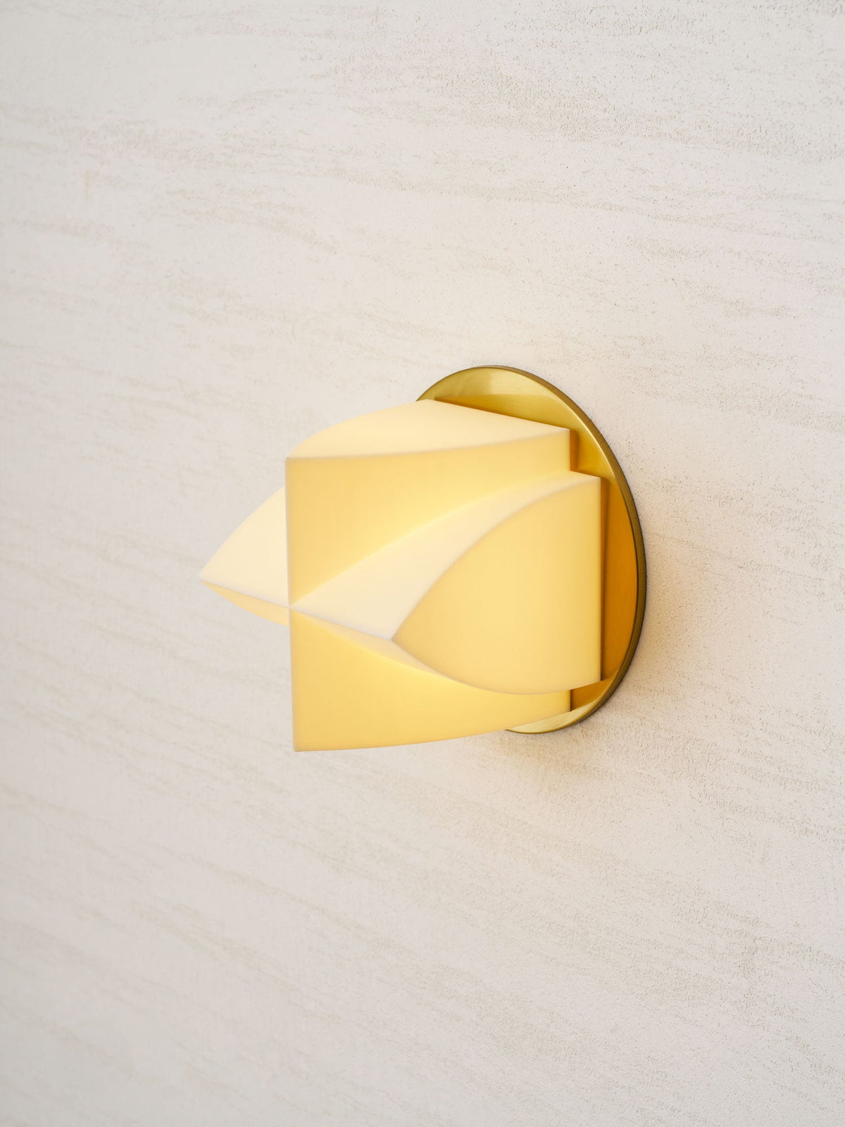 Close angled view of a lit Clérachic wall sconce, its white facets glowing yellow in front of a gold backplate.