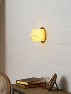 A small lit Clérachic sconce on a white wall above a wooden console with books, a glass goblet and an oval picture.