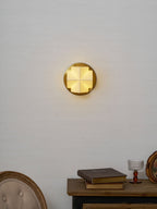 A Clérachic wall sconce lit warm and centred on a pale wall, above a console with books and a glass on a stem.