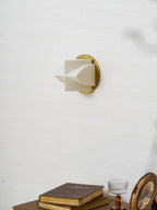 An unlit Clérachic sconce in profile on a white wall, with a stack of books and a round gilt frame below.