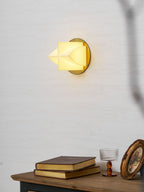 A Clérachic sconce lit yellow in profile, with a stack of books, a glass and a gilt frame on the console below.