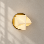 Close, angled view of a lit Clérachic wall sconce on a beige wall, with sunlight and window shadows falling across it.