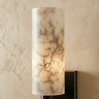 Close view of the Clérachic alabaster wall sconce's veined stone shade, lit from within to show its natural markings.