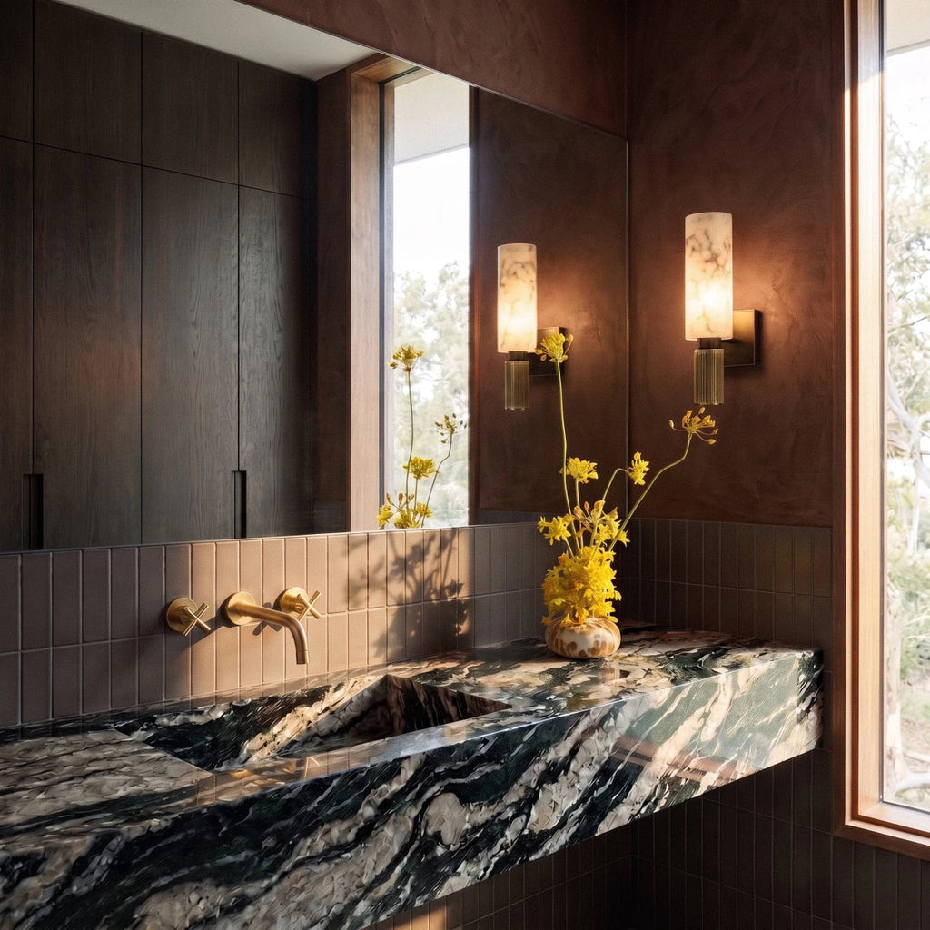 Pair of Clérachic alabaster wall sconces flanking a mirror above a dark stone bathroom vanity with fresh flowers.