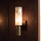 Clérachic gold alabaster wall sconce glowing against a deep rust-toned plaster wall near a timber door frame.