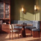 Two Clérachic alabaster wall sconces light an olive green dining nook above a striped banquette and round table.
