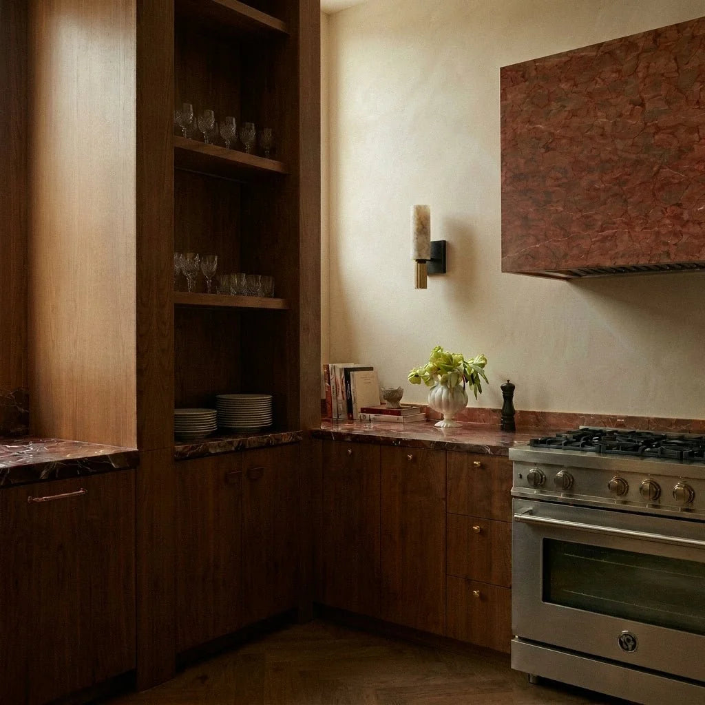 Clérachic alabaster wall sconce mounted beside a stone range hood in a warm kitchen with open glassware shelving.