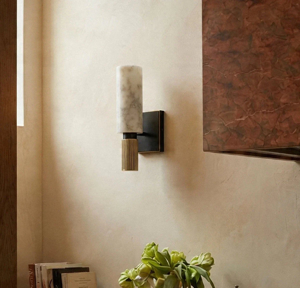 Detail of the Clérachic alabaster sconce on a cream wall beside a stone hood corner, books and greenery below.