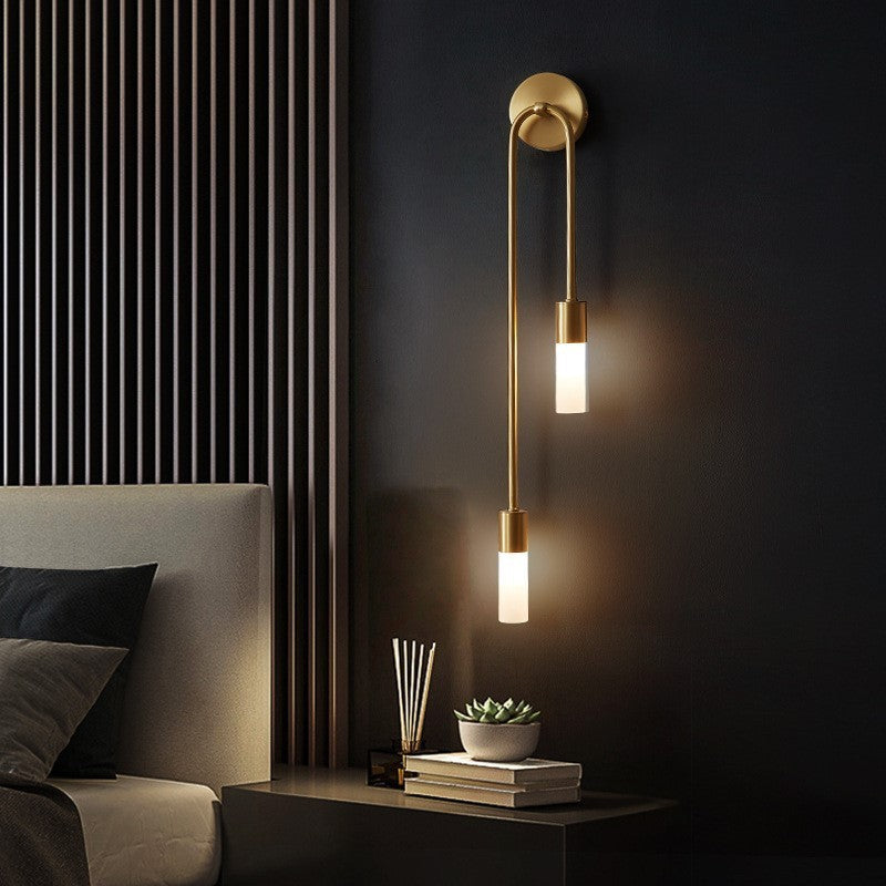 Clérachic's gold stick sconce mounted above a bedside table, its two frosted shades glowing warm white.