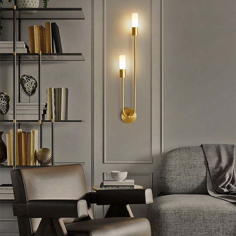 Clérachic's gold stick sconce mounted beside an open bookshelf, its frosted shade glowing softly.